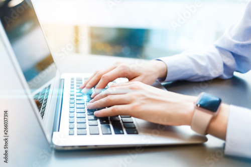 Business woman working in modern sunny office on modern laptop. Closeup of female hands typing on notebook keyboard. Toned. Light blurred background. Concept of new technology