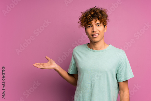 Young african american man over isolated purple wall holding copyspace imaginary on the palm