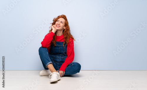 Redhead woman with overalls sitting on the floor thinking an idea while looking up