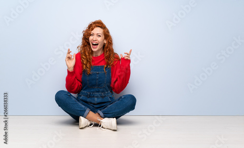 Redhead woman with overalls sitting on the floor smiling a lot