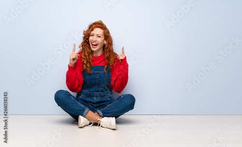 Redhead woman with overalls sitting on the floor pointing up a great idea