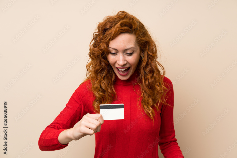 Redhead woman with turtleneck sweater holding a credit card