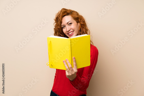 Redhead woman with turtleneck sweater holding and reading a book