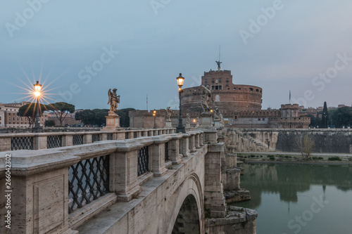 Lateral view Stone bridge with historic illumination over the Tiber at dawn. Aurelius bridge with the Castle Sant Angelo in the background in the center of the historic center of Rome.