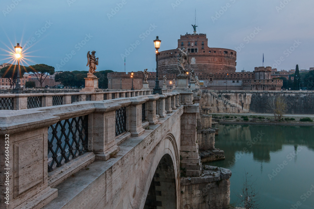 Fototapeta premium Aurelius bridge with the Castle Sant Angelo in the morning at dusk. Lateral view of the stone bridge. Historic streets lighting on the bridge over the river Tiber in Rome.