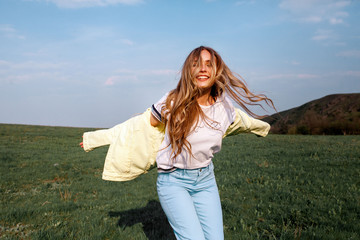 Outdoors lifestyle fashion portrait of happy smilling blonde girl. Beautiful smile. Long curly light hair. Wearing stylish yellow jacket and jeans. Joyful and cheerful woman. Happiness
