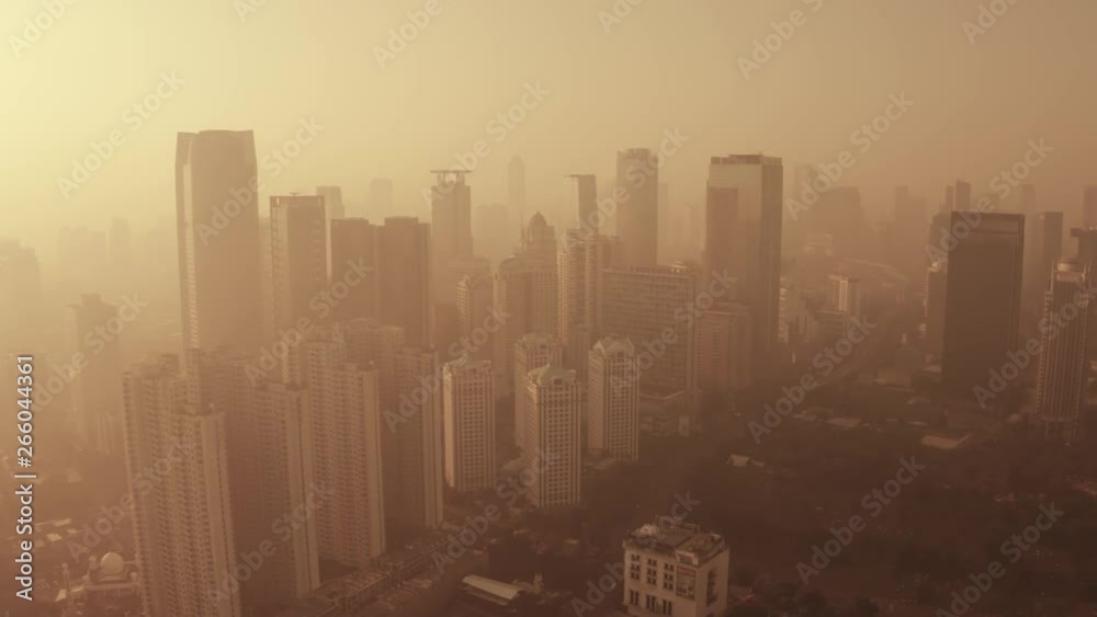 JAKARTA, Indonesia - May 02, 2019: Aerial landscape of silhouette of apartment and office building behind fog of air pollution with orange sky. Shot in 4k resolution from a drone flying forwards JAKARTA, Indonesia - May 02, 2019: Aerial landscape of silhouette of apartment and office building behind fog of air pollution with orange sky. Shot in 4k resolution from a drone flying forwards