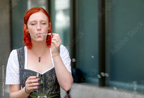 Tableau sur toile Young pretty redhead ginger girl making rainbow bubbles wearing a dirndl at a we