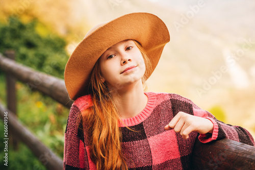 Fotografie Outdoor close up portrait of pretty young red-haired girl wearing brown hat