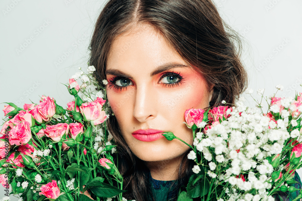 Studio shot of beautiful woman with long dark hair, bright pink makeup, wearing green dress, holding small roses bouquet Studio shot of beautiful woman with long dark hair, bright pink makeup, wearing green dress, holding small roses bouquet