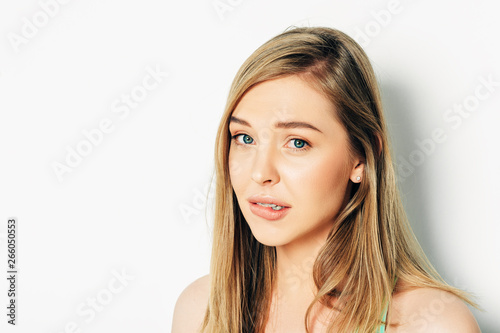 Close up portrait of beautiful young woman with blond hair and nude make up, guilty facial expression, biting lip