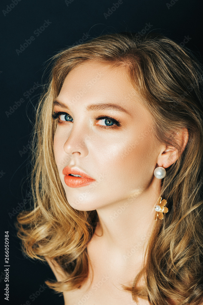 Fototapeta premium Close up portrait of beautiful young woman with blond hair and professional make up, posing on black background