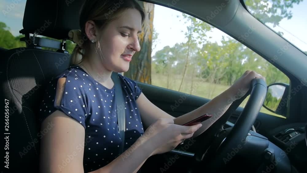 Slow motion footage of young woman using smartphone while driving a car. Please use handsfree in vehicle for your safety