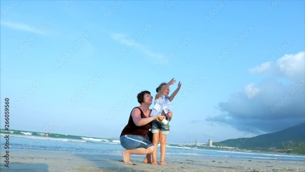 Happy grandmother with child the playing flying kite, the family runs on the sand of a tropical ocean playing with the older kite. Concept Happy and carefree childhood. Happy grandmother with child the playing flying kite, the family runs on the sand of a tropical ocean playing with the older kite. Concept Happy and carefree childhood.