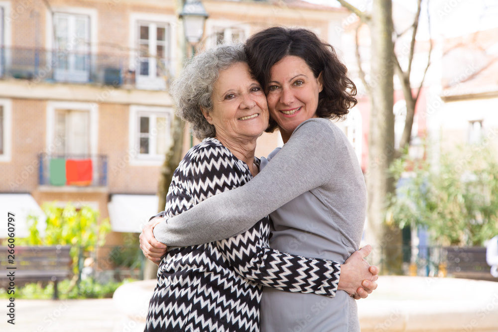 Fototapeta premium Happy positive young woman posing with her mom. Mother and daughter enjoying walking outdoors and hugging each other. Family love concept