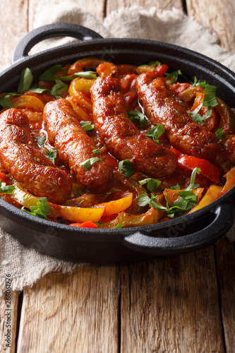 Delicious Italian sausages grilled with bell peppers, onions and tomatoes close-up in a frying pan. vertical
