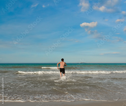 Obraz na płótnie A man runs into the water of the tropical sea. View from the back. Copy space for text. Vietnam w salonie