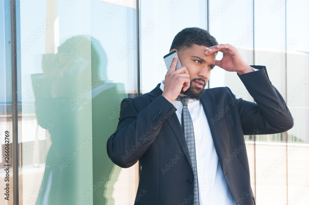Concerned businessman speaking on phone outdoors and getting bad news. Young Latin man in suit and tie touching head with upset face and talking on cell outside. Business troubles concept Concerned businessman speaking on phone outdoors and getting bad news. Young Latin man in suit and tie touching head with upset face and talking on cell outside. Business troubles concept