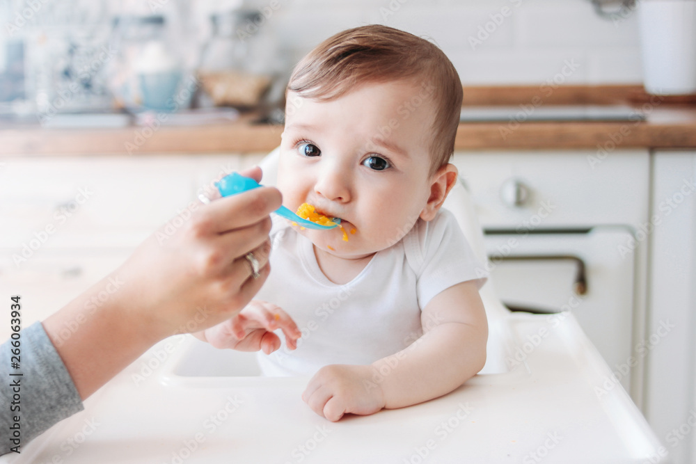 Charming little baby boy 6-8 months eating first food pumpkin from spoon at home Charming little baby boy 6-8 months eating first food pumpkin from spoon at home