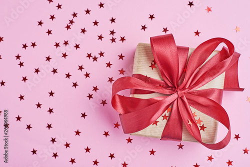 Gift box wrapped in kraft paper with red bow and confetti in shape star on pink background, close up © Lazy_Bear