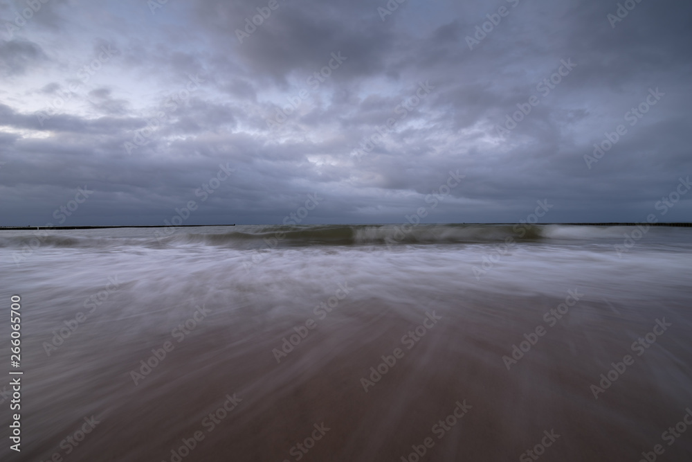 Sunset on the beach with waves against a dramatic blue cloudy sky, baltic sea, Usedom