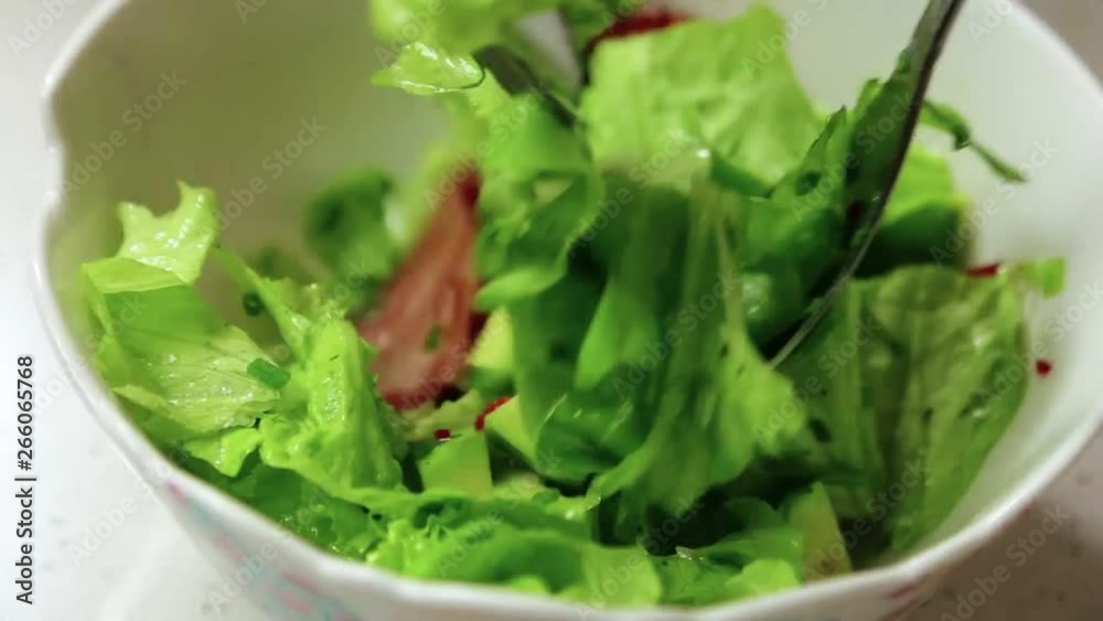 Person preparing mixing salad ingredients in a white bowl with two forks. Yummy green salad oil and bacon. Person preparing mixing salad ingredients in a white bowl with two forks. Yummy green salad oil and bacon.