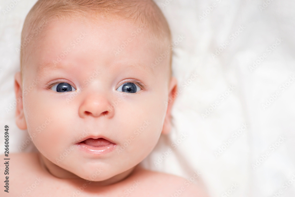 Little newborn baby boy lying in white clothes on white blanket background. Cute baby girl makes a funny upset face isolated on a white background