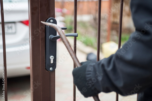 Burglar trying to break the gate with a crowbar. Burglar trying to force a lock using a crowbar