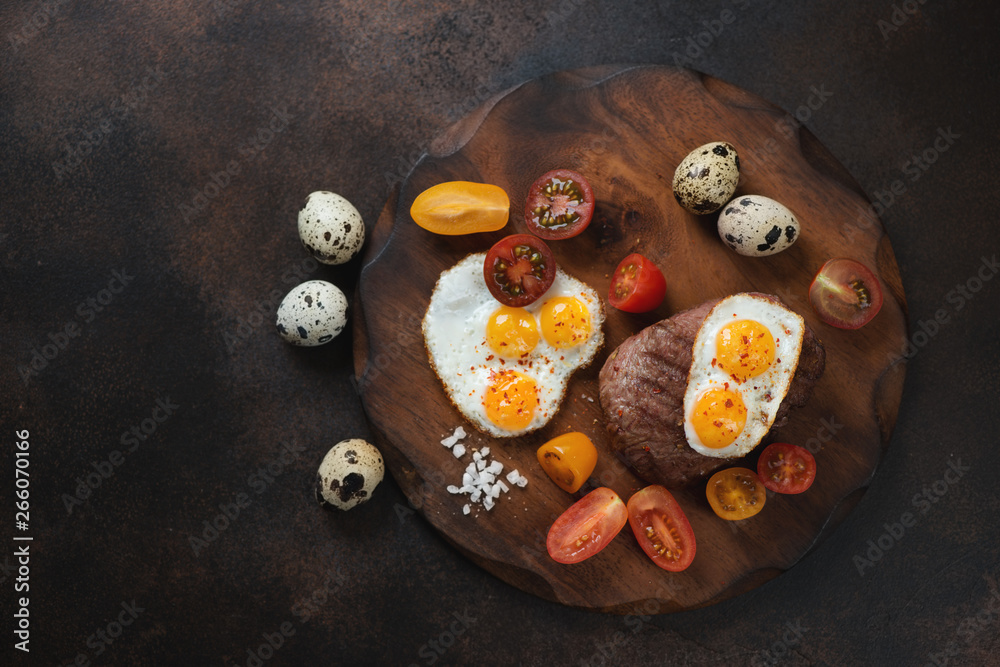 Grilled marbled beefsteak in tuscan style - with fried quail eggs and cherry tomatoes. Flatlay on a dark brown metal background with space Grilled marbled beefsteak in tuscan style - with fried quail eggs and cherry tomatoes. Flatlay on a dark brown metal background with space