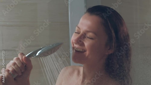Young beautiful woman in the shower. Glass cabin. Hot shower, steam and drops on the walls Sings in the watering can shower. Relaxation.