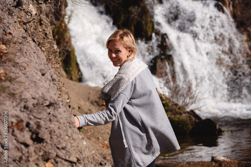Portrait of a blonde Girl in a stylish jacket on the background of a waterfall. The concept of travel.