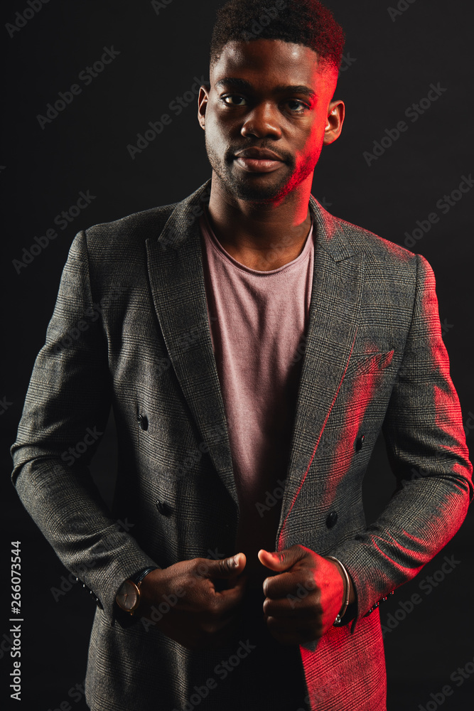Successful young dark-skinned entrepreneur in formal clothing, standing against dark purple background, thinking and making plans for future, while relaxing after hard day in the office