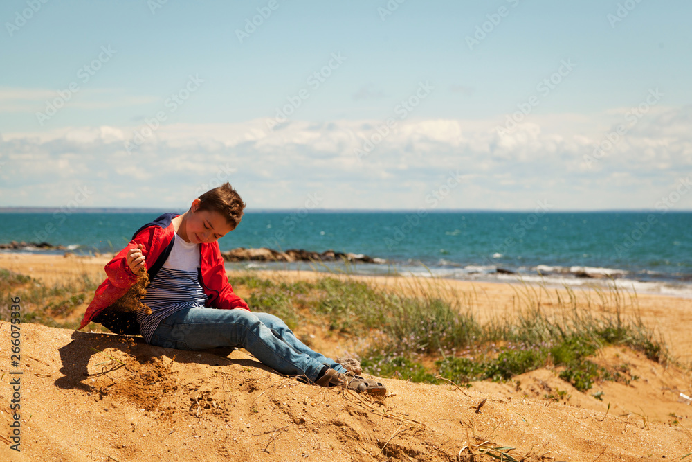 Teenager sits on the sand by the sea