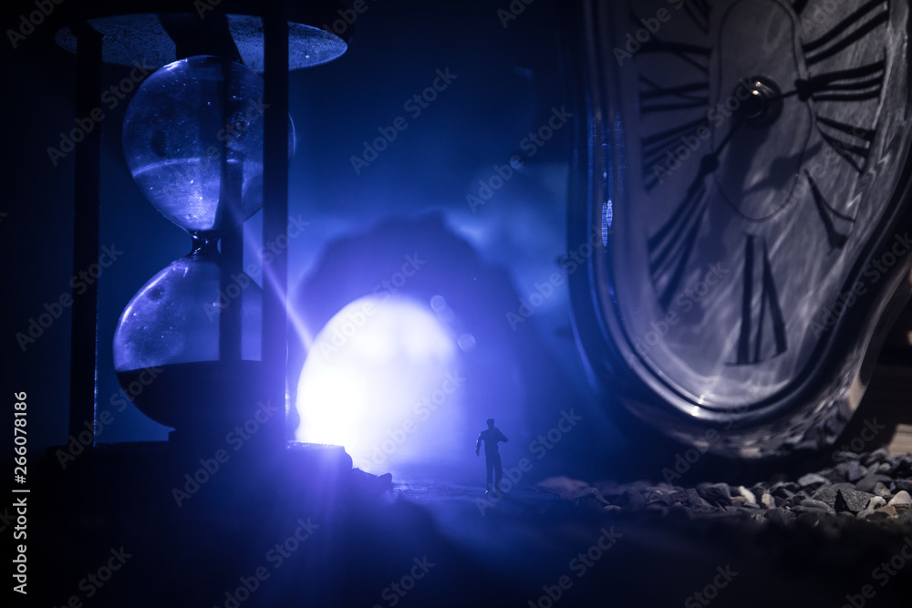 Time concept. Silhouette of a man standing between hourglasses with smoke and lights on a dark background. Surreal decorated picture Time concept. Silhouette of a man standing between hourglasses with smoke and lights on a dark background. Surreal decorated picture