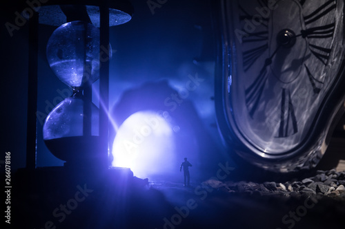 Time concept. Silhouette of a man standing between hourglasses with smoke and lights on a dark background. Surreal decorated picture