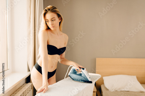 sexy blonde undressed maid ironing clothes in sunny morning at home. Woman  dressed in black bra and panties. Stock Photo | Adobe Stock