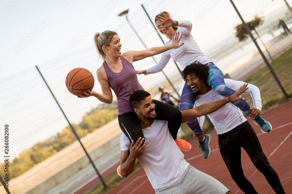 Obraz premium Young women sitting on the men shoulders and holding a basketball at outdoor court