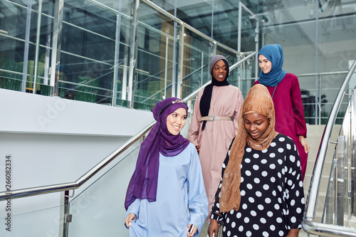 Group of smiling muslim women in hijab walking down the stairs of business centre. Arabian and african ladies dressed in long smart dresses and scarfs going to conference hall