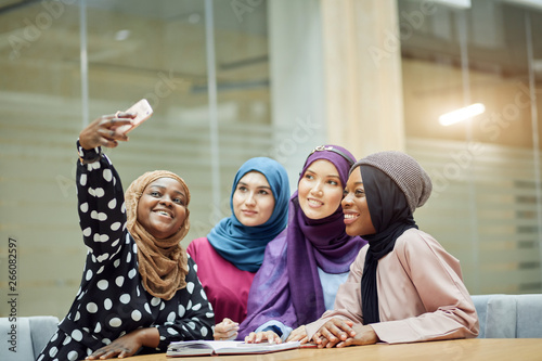 Canvas Print Asian Islamic women in bright hijabs sharing info from smartphone during their v