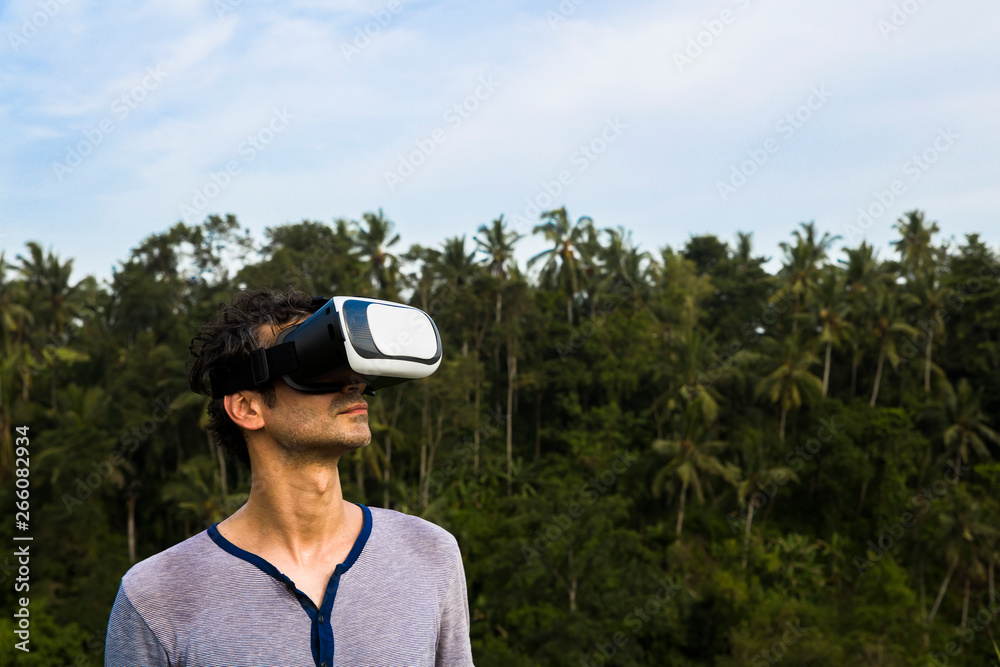 Young man with VR glasses in the tropical forest