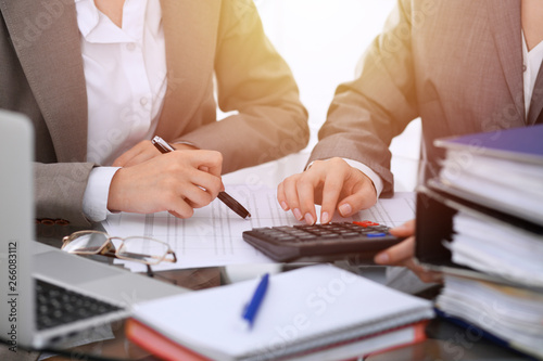 Two female accountants counting on calculator income for tax form completion hands close-up. Business and audit concept
