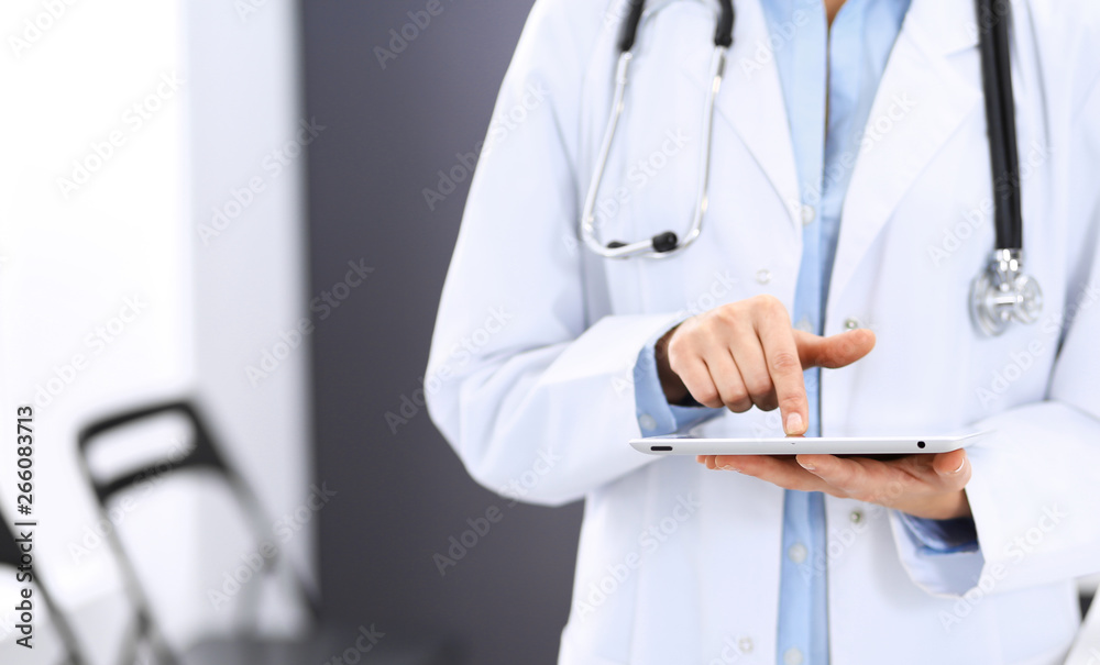 Female physician using digital tablet while standing near reception desk at clinic or emergency hospital. Unknown doctor woman at work. Medicine concept Female physician using digital tablet while standing near reception desk at clinic or emergency hospital. Unknown doctor woman at work. Medicine concept