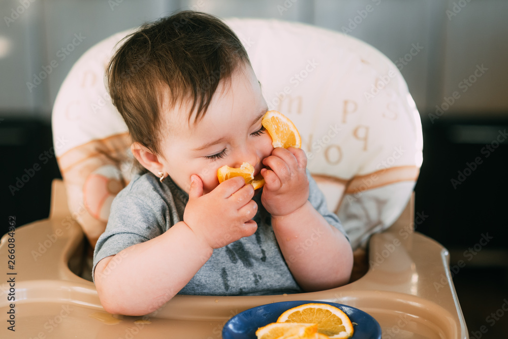 little girl sitting in baby chair, eating an orange little girl sitting in baby chair, eating an orange
