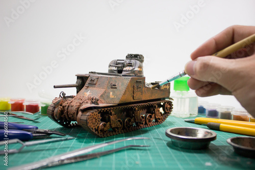 Painting plastic model WW2 tank M3 Lee with part and tools on wooden workbench closeup. 