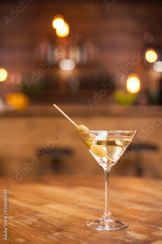 Green olives on a stick in a glass of dry martini over a rustic wooden table