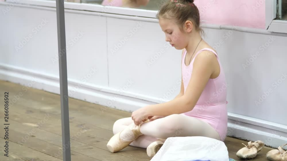teen little girl in a pink leotard, prepares for classical ballet dance lesson in a ballet school. she putting on her pointe shoes, sitting on an old wooden floor, teen little girl in a pink leotard, prepares for classical ballet dance lesson in a ballet school. she putting on her pointe shoes, sitting on an old wooden floor,