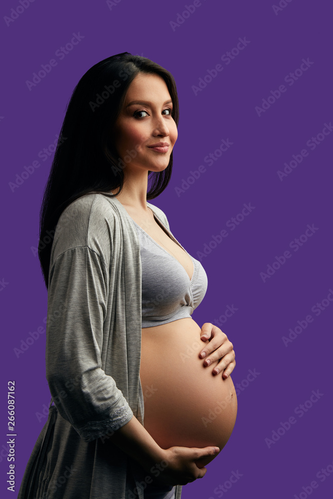 Long Hair Pregnant Nude - Studio portrait of pregnant caucasian woman with long dark hair. Happy  future Mom posing with hands on naked belly over purple background Photos |  Adobe Stock