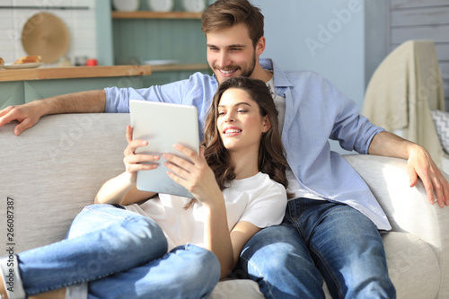 Young couple watching media content online in a tablet sitting on a sofa in the living room. photo