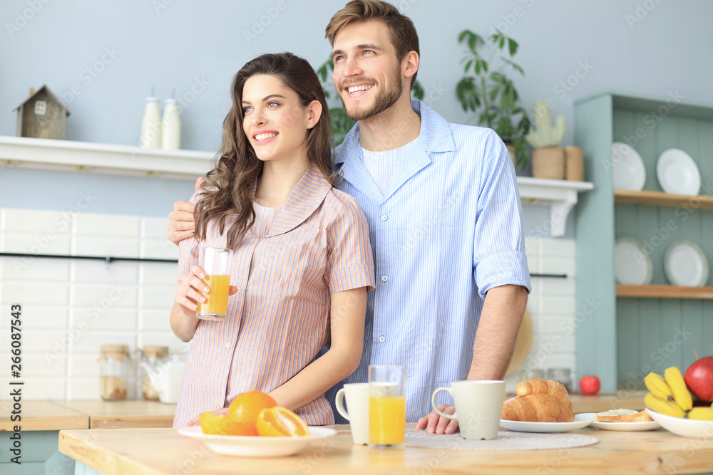 Portrait of happy young couple in pajamas cooking together in the kitchen, drinking orange juice in the morning at home.
