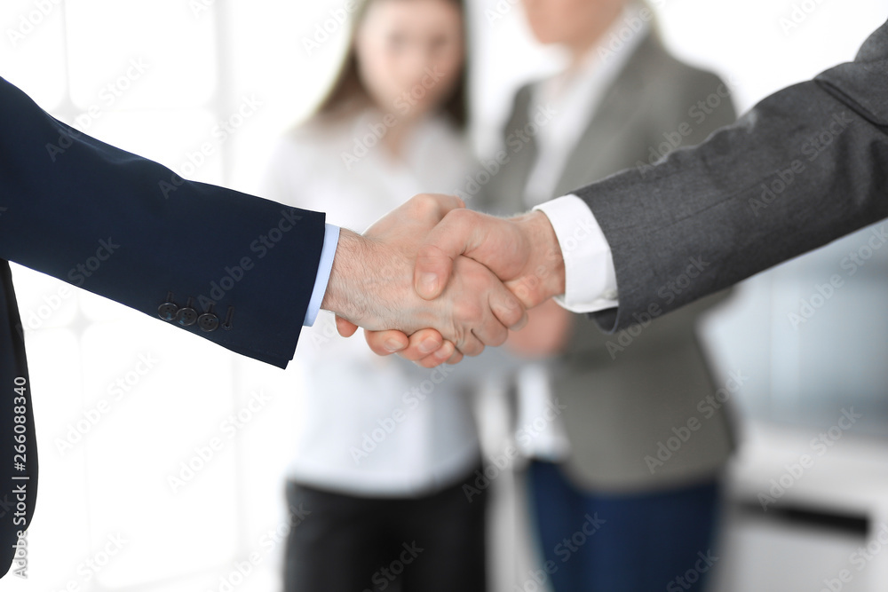 Business people shaking hands at meeting or negotiation, close-up. Group of unknown businessmen and women in modern office at background. Teamwork, partnership and handshake concept